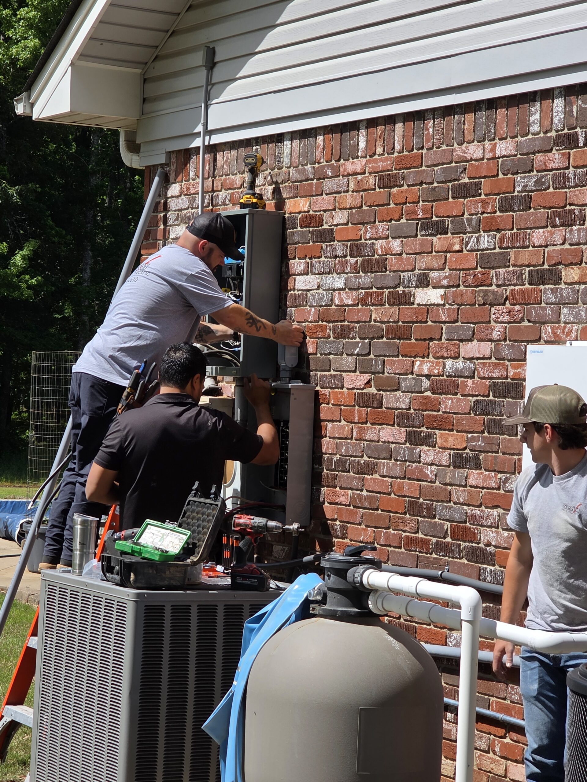 20260508_105025 - Adam Tull Three members of the electrical team working on a breaker panel outside a brick house.